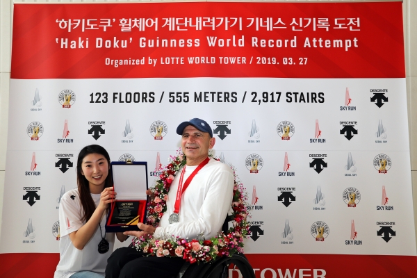 롯데월드타워 123층부터 2,917계단을 49분 56초 기록으로 내려온 하키도쿠 선수에게 ‘스카이런(SKYRUN)’ 인증패를 전달하고 있다.